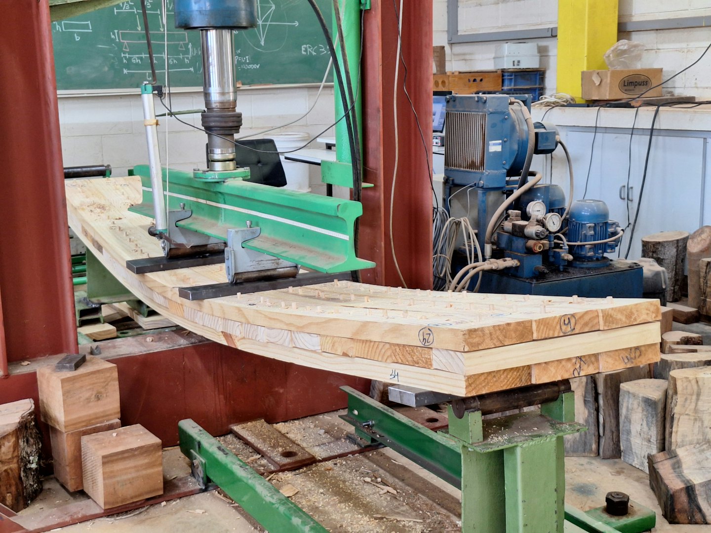 Green hydraulic press testing a timber beam in a workshop.