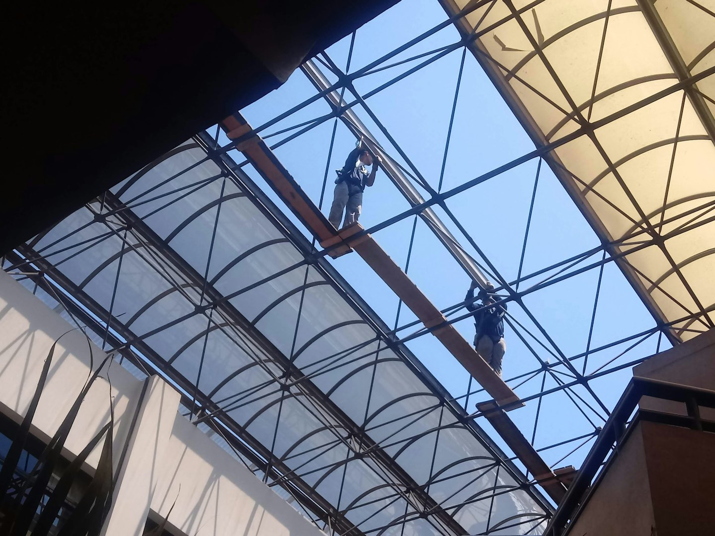 Workers installing a skylight on a building under a blue sky.